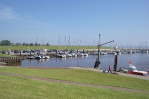 A marina with boats docked, a grassy area, and a small boat on the water. - Guesthouse "Am Tief" for up to 5 people (Wangerland)