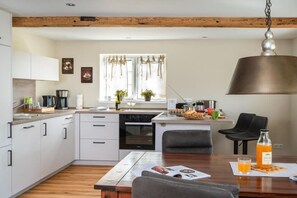 A modern kitchen with white cabinets, a wooden ceiling, and a hanging pendant light. - White Cottage Estate Priesholz (Rabenholz)