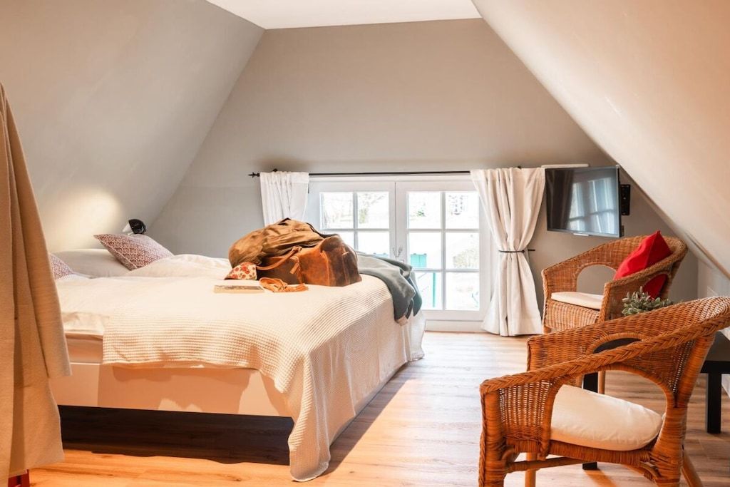 A bedroom with a bed, a chair, a window, and a flat-screen TV.