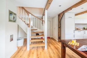 Eine Treppe mit Holzboden und weißen Geländern führt zu einem Küchenbereich mit weißen Schränken und einem Holztisch.