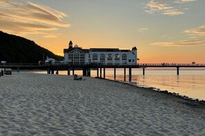 A beach with a pier and a building with arched windows. - Villa Louisa 46 - Störtebeker (Ostseebad Sellin)