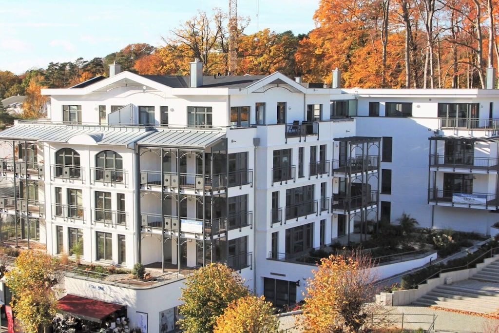 Un edificio a più piani con balconi e ampie finestre, circondato da alberi con foglie autunnali.