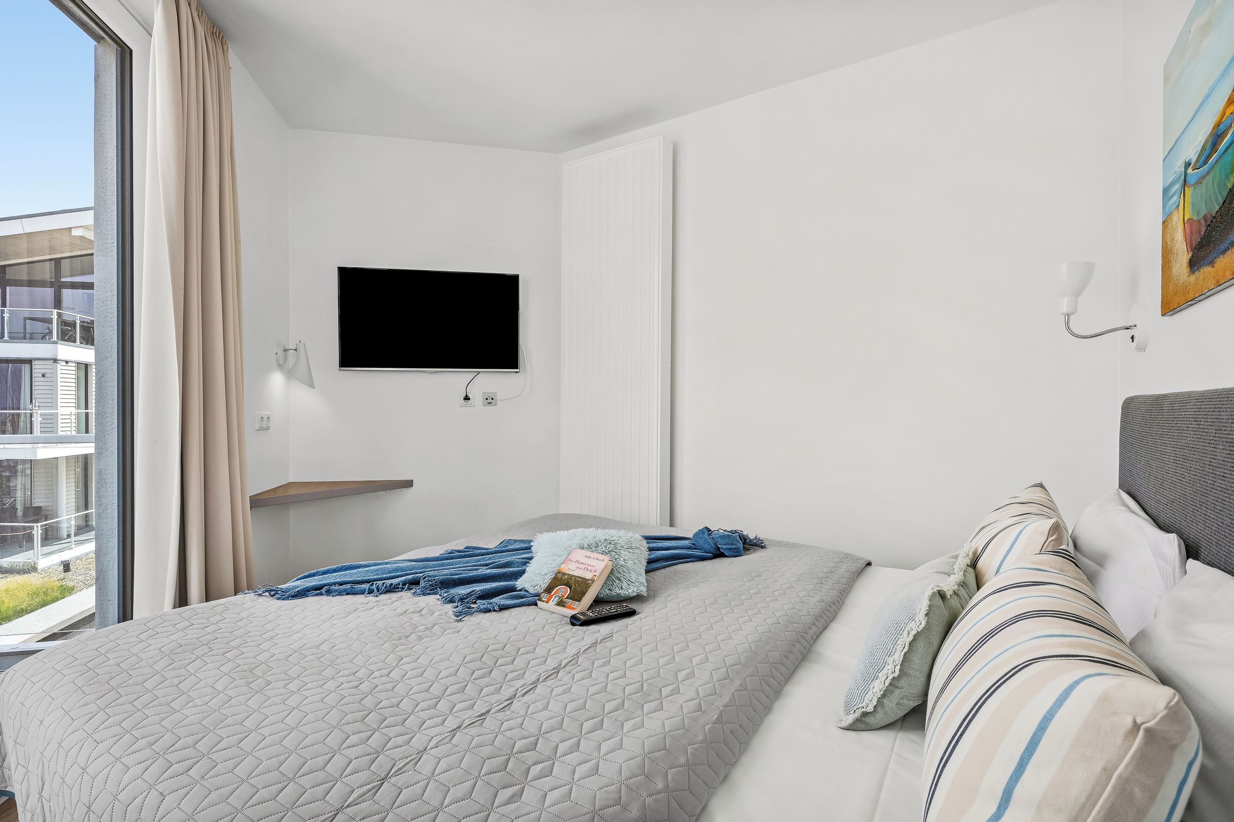 Ein Hotelzimmer mit einem Bett, einem an der Wand montierten Fernseher und einem Fenster mit Vorhängen.