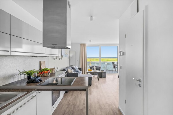 A modern kitchen with a central island, a dining area with a view, and a balcony with a view. - Kielwasser – Prime Location, Stunning Sea Views, Steam Shower & Private Parking (Wendtorf)
