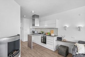 A modern kitchen with white cabinets, a central island, and a built-in oven. - Kielwasser – Prime Location, Stunning Sea Views, Steam Shower & Private Parking (Wendtorf)