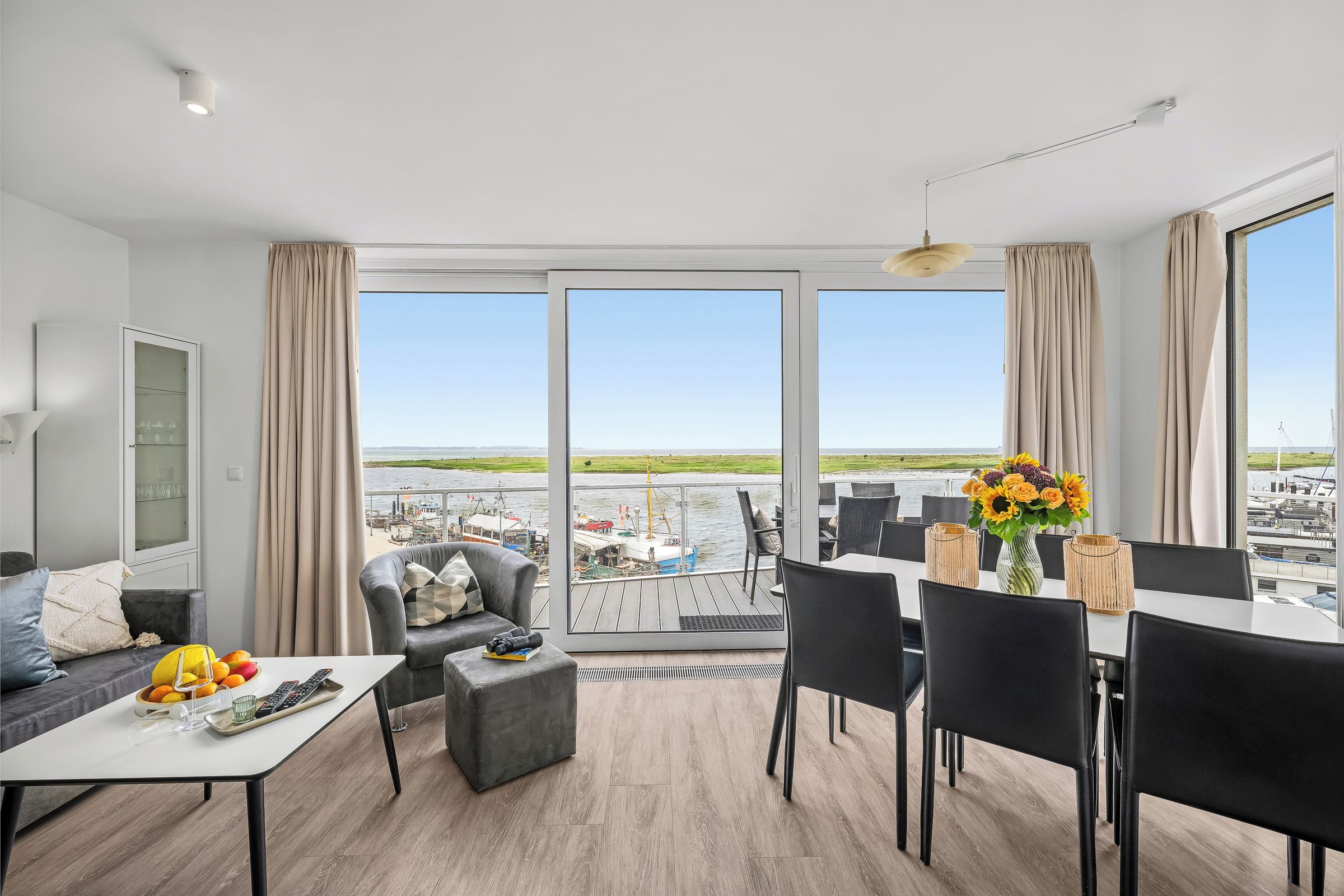 Un salon moderne avec un coin repas, de grandes fenêtres et une vue sur le port.