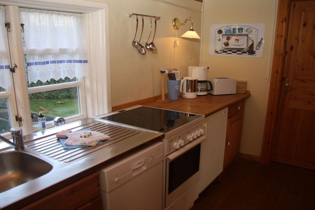 A compact kitchen with a sink, stove, and a window with a view of greenery.
