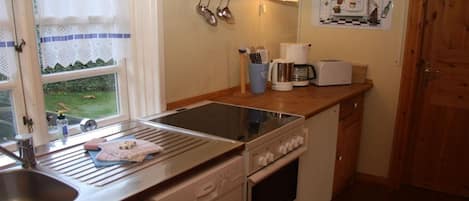 A compact kitchen with a sink, stove, and a window with a view of greenery.