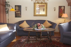 A living room with a blue sofa, a round coffee table with a floral centerpiece, and a patterned rug. - Keitumer Chaussee 5 Holiday Apartment 2 (Sylt Westerland)