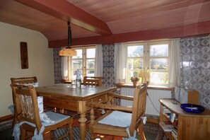 A dining area with a wooden table and chairs, a hanging light fixture, patterned wallpaper, and a view of the outdoors through windows. - Keitumer Chaussee 5 Holiday Apartment 2 (Sylt Westerland)