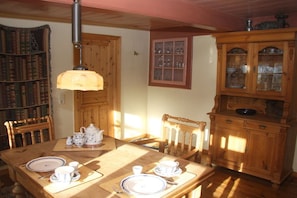 A dining area with a wooden table set for four, a bookshelf, and a cabinet with glass doors. - Keitumer Chaussee 5 Holiday Apartment 2 (Sylt Westerland)