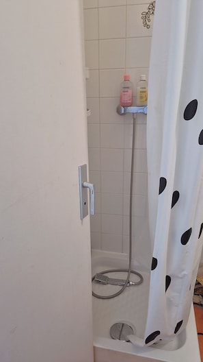 Un angolo doccia con tenda bianca a pois neri, un soffione a mano e due flaconi di shampoo su uno scaffale.