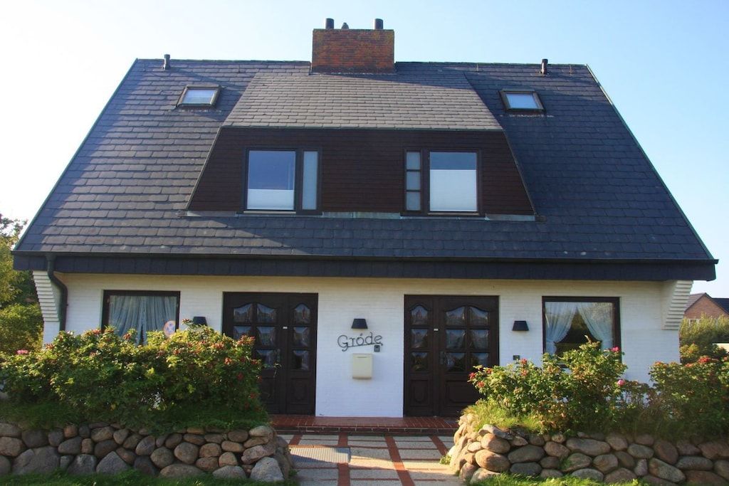 A two-story house with a dark roof, a chimney, and a sign that reads 'Gröde'.