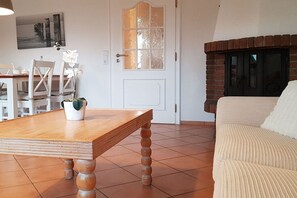 A living room with a wooden table, a white sofa, a fireplace, and a door with frosted glass panels. - House Oland Holiday Apartment 5 (Wenningstedt)
