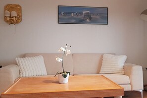 Ein Wohnzimmer mit einem beigefarbenen Sofa, einem Holztisch und einer Topf-Orchidee.