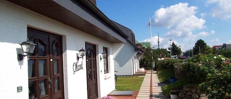 Ein Gebäude mit heller Fassade, braunen Türen und einem Weg zum Eingang.