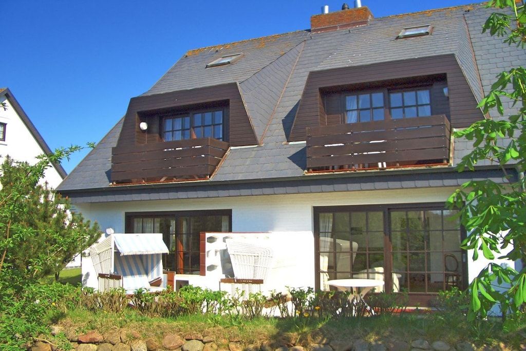 A house with a sloped roof, large windows, and a small garden area with outdoor furniture.