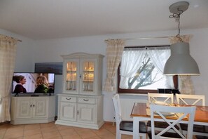 A dining area with a table, chairs, a cabinet, and a television. - House Oland Holiday Apartment 5 (Wenningstedt)