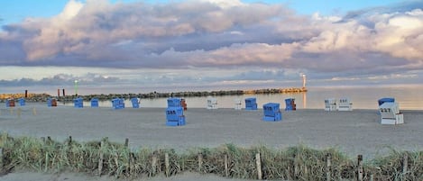 A beach with numbered blue chairs and a lighthouse in the distance.
