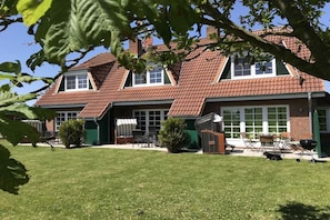 Ein zweistöckiges Haus mit geneigtem Dach, einer überdachten Terrasse und einem gepflegten Rasen.
