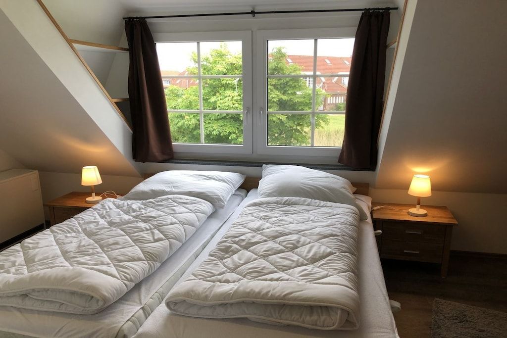 A bedroom with two beds, a window with curtains, and bedside lamps.