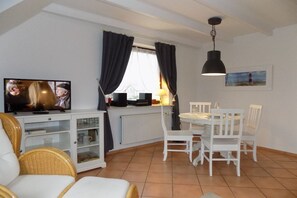 Un salon avec un téléviseur, des meubles blancs, une table à manger et une fenêtre avec des rideaux.