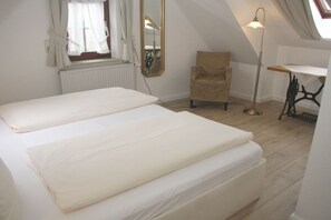 Ein Schlafzimmer mit zwei Betten, einem Sessel, einem Tisch, einem Spiegel und einer Heizung.