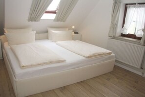 Une chambre avec un grand lit, une table de chevet, une fenêtre avec des rideaux et un radiateur.