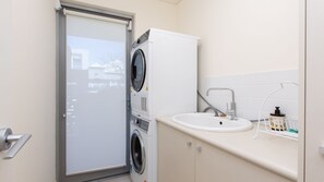 Una lavanderia compatta con lavatrice e asciugatrice a carica frontale, un lavandino con rubinetto e una piccola finestra con vista su un edificio.