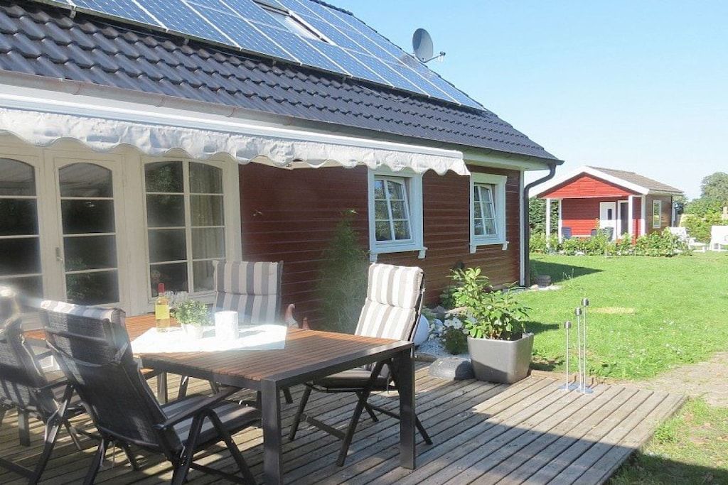 A wooden deck with a table and chairs, a potted plant, and a house with solar panels.