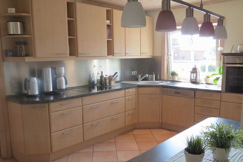 Een moderne keuken met houten kastjes, een zwart aanrecht en hanglampen.