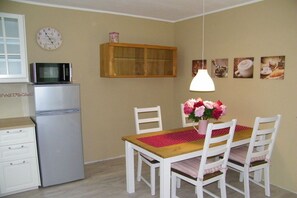 Eine kompakte Küche mit Kühlschrank, Mikrowelle, Holzschrank und Esstisch mit Stühlen.