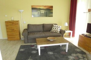 Ein Wohnzimmer mit einer Couch, einem Couchtisch, einem Bild an der Wand, einer Lampe und einem Fernseher.