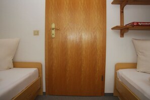 A room with two wooden beds, a wooden door, and a shelf with a box. - Holiday apartment in Sylt with 2 bedrooms (Westerland)