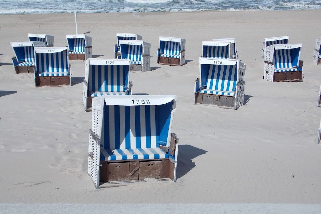 Des chaises de plage, chacune portant un numéro, sont disposées sur une plage de sable.
