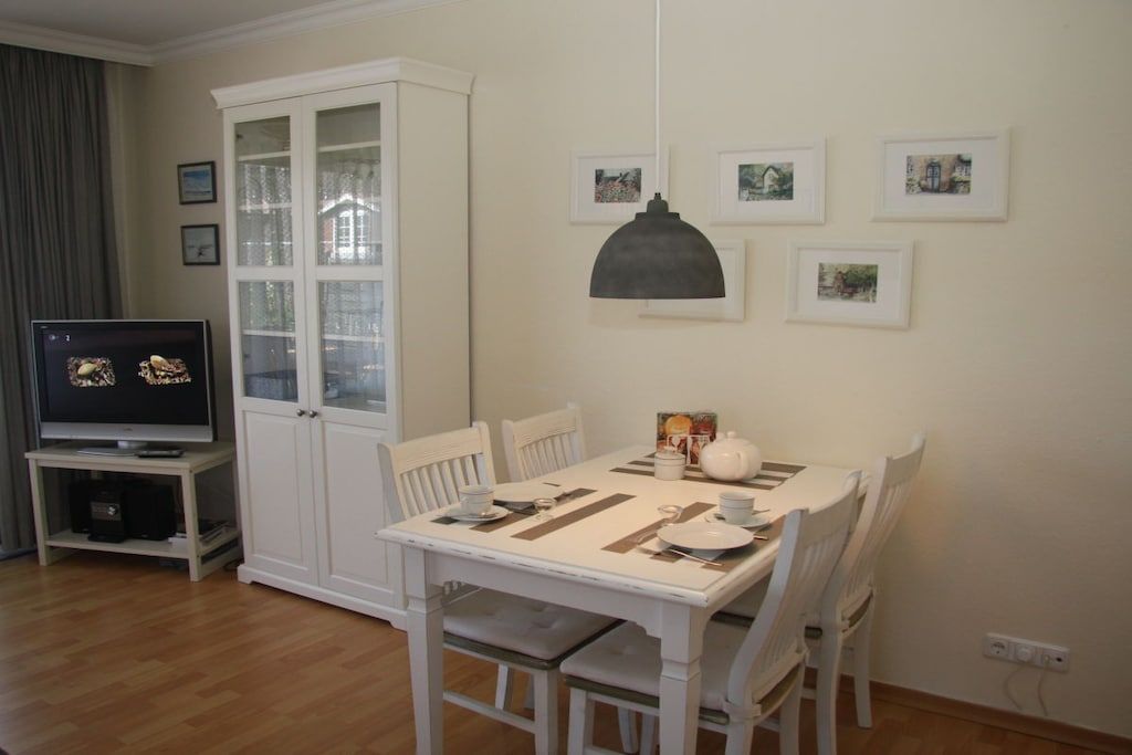 Een eethoek met een witte tafel gedekt voor vier personen, een kast met glazen deuren en een televisietoestel op een meubel.