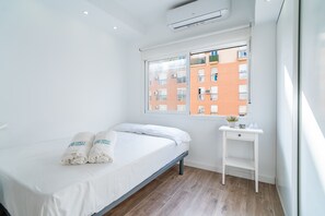 Ein Hotelzimmer mit Bett, Nachttisch, Fenster mit Blick auf Gebäude und Klimaanlage.