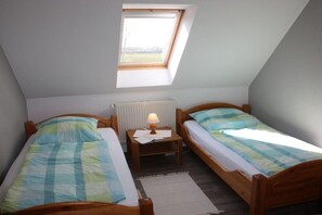 Ein kleiner, dreieckiger Raum mit zwei Holzbett, einem Nachttisch mit Lampe und einem Fenster, das für natürliches Licht sorgt.
