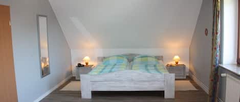 A bedroom with a bed, two bedside lamps, a mirror, and a radiator.