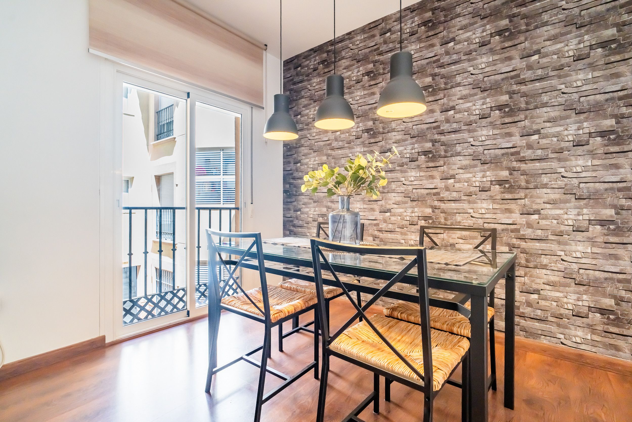 Een eethoek met een glazen tafel en stoelen, een stenen muur en hanglampen.