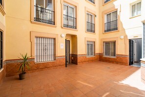 A courtyard with tiled flooring, a potted plant, and a building with barred windows and balconies. - Cubo's Montaño Malaga Apartment / near beach / urban / air conditioning / free wifi (Málaga)