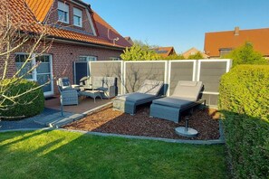 A backyard with a brick house, a patio with outdoor furniture, and a well-maintained lawn. - Holiday home in Hage with swimming pool (Hage)