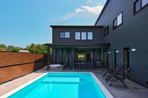 Una casa moderna con piscina, mobiliario exterior y un patio cubierto.