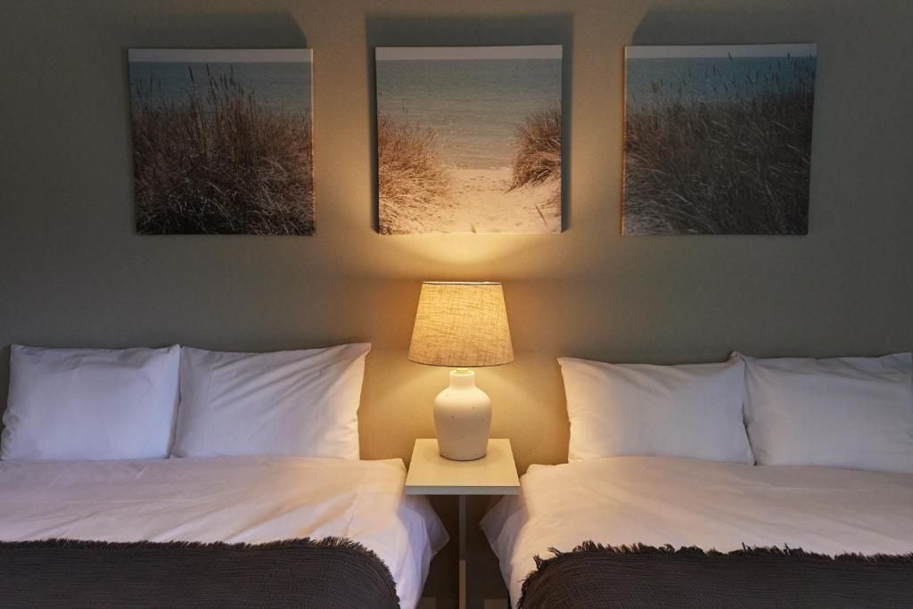 Habitación de hotel con dos camas, una mesita de noche con lámpara y tres obras de arte con temática de playa.