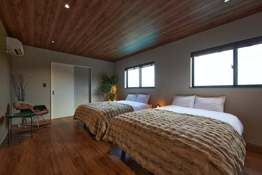 Quarto com duas camas, uma escrivaninha e uma cadeira. Há janelas e uma porta.