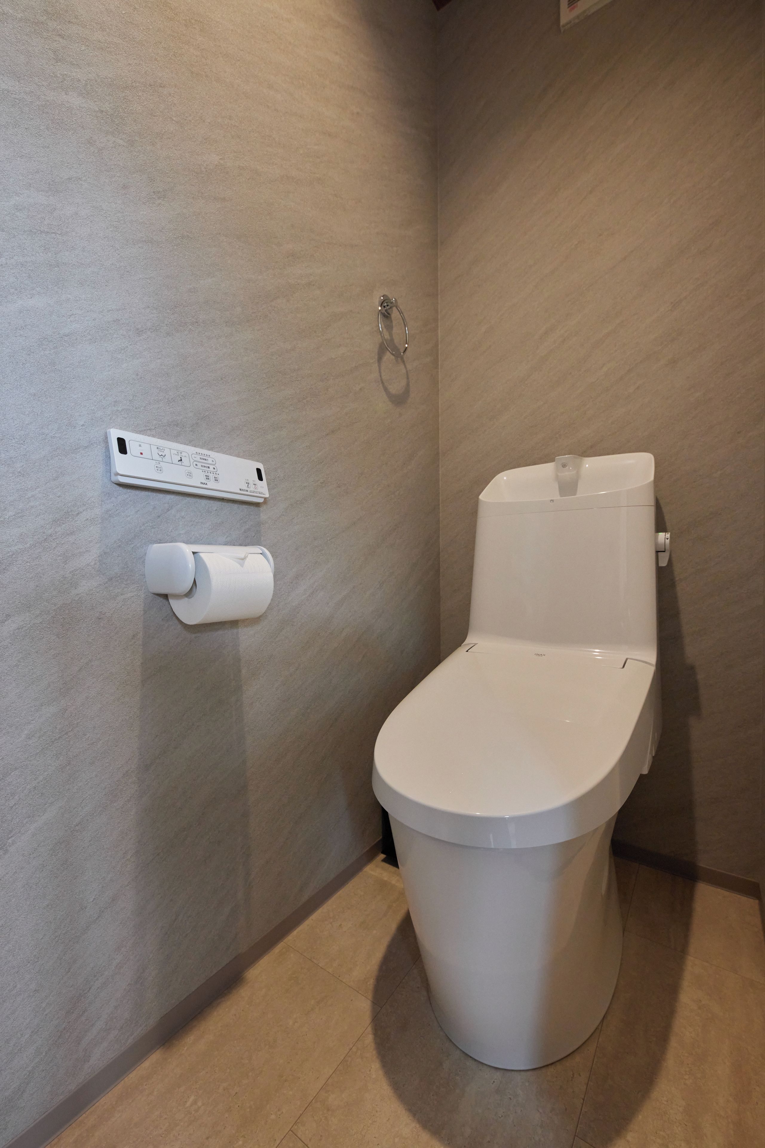 A modern bathroom with a toilet, a toilet paper holder, and a wall-mounted control panel.