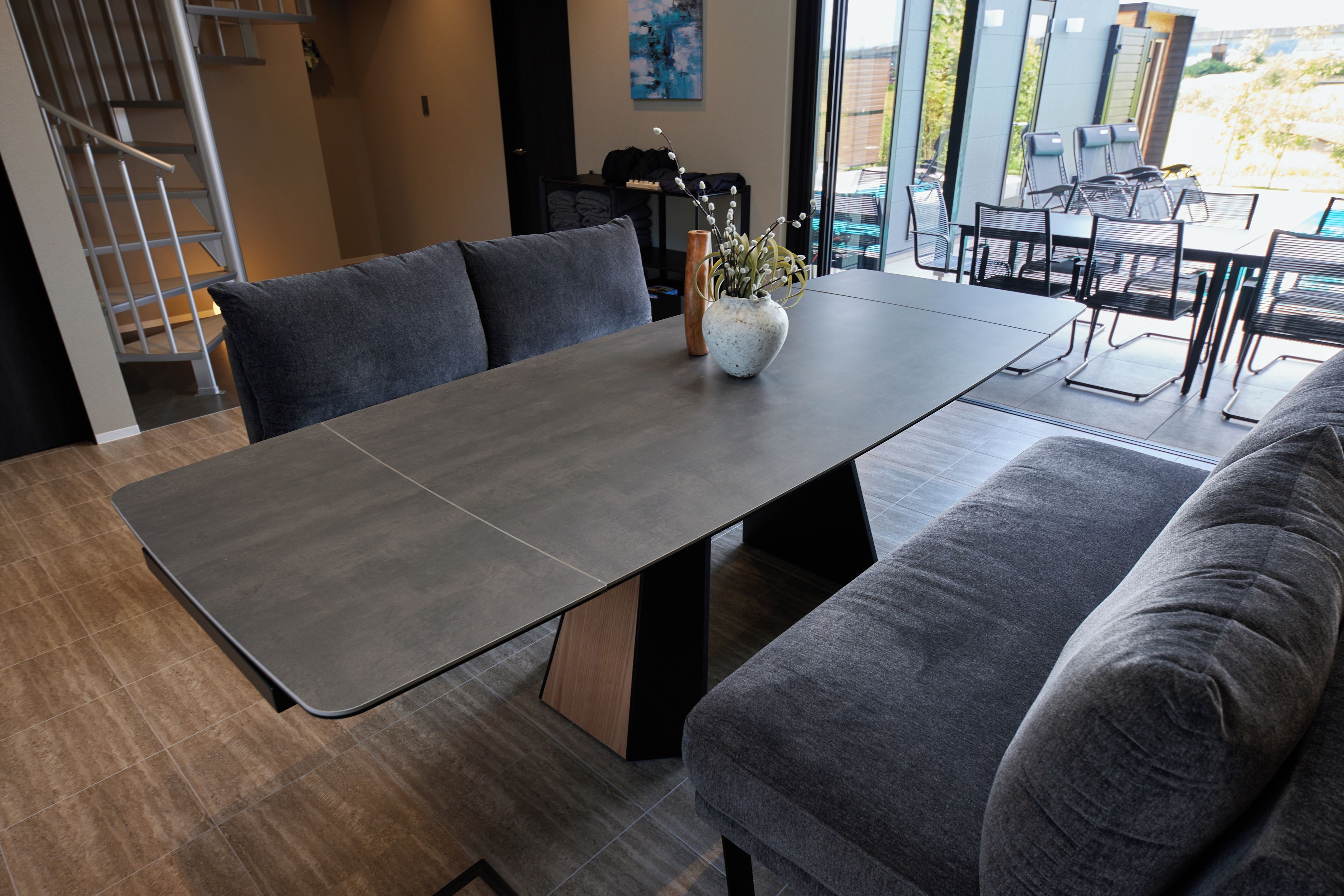 A modern dining area with a long table, cushioned seating, and a vase with flowers.