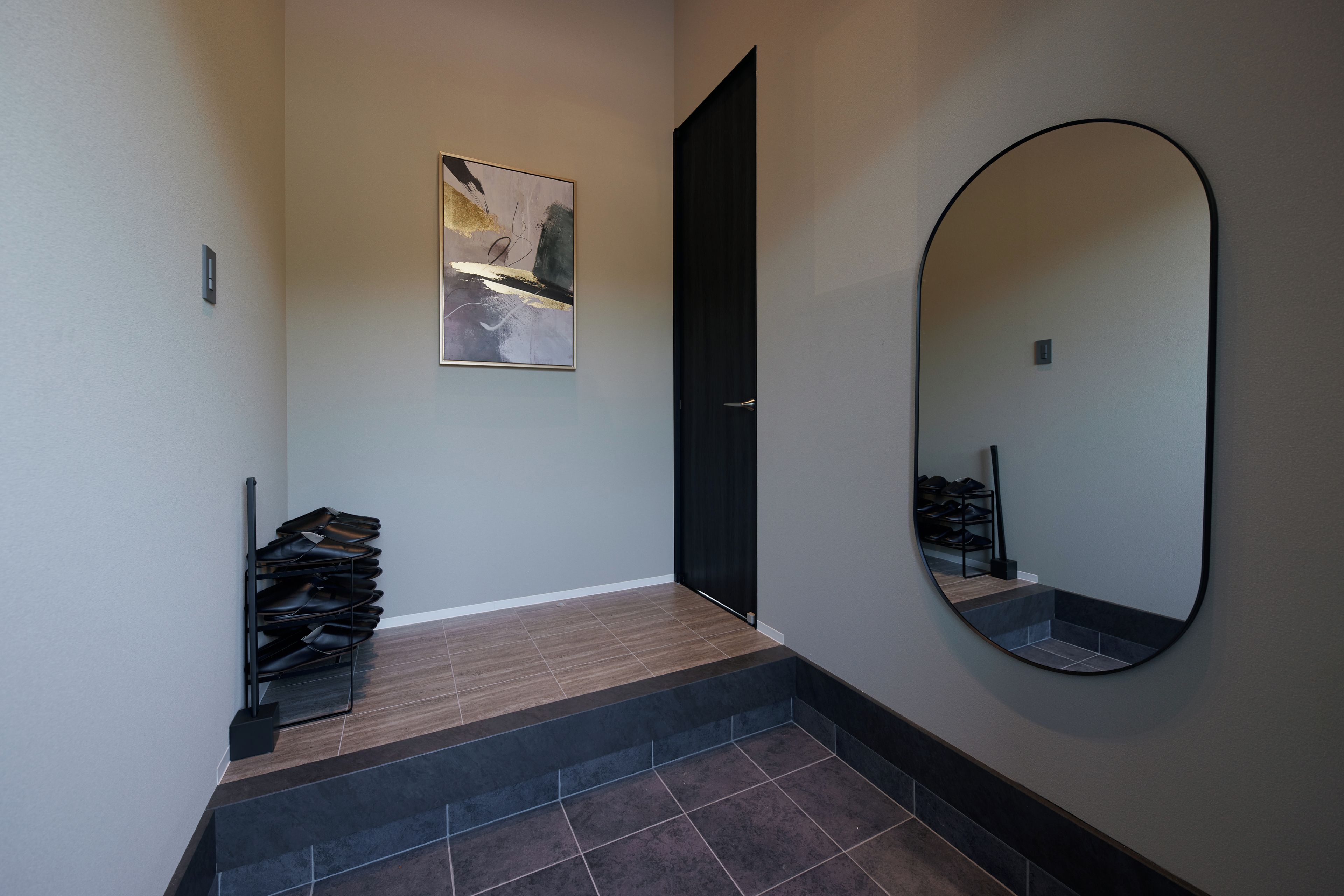 Un couloir avec un meuble à chaussures, une porte, un tableau abstrait encadré et un grand miroir.