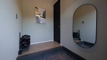 Un couloir avec un meuble à chaussures, une porte, un tableau abstrait encadré et un grand miroir.