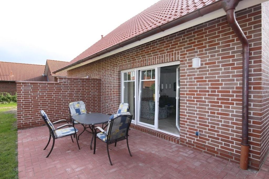 Un patio con una mesa, sillas, un muro de ladrillo y una puerta corrediza de vidrio.